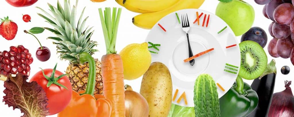 głodówka lecznicza, post przerywany zilustrowany jako zegar wykonany z talerz i sztućców otoczonych kolorowymi warzywami i owocami