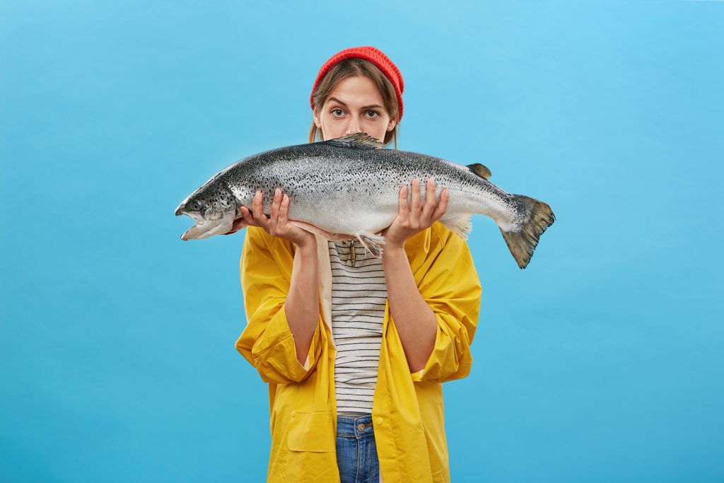 zdjęcie: młoda kobieta na wysokości twarzy trzyma dużą rybę. ich spożywanie pozytywnie wpływa na poziom witaminy d w ludzkim organizmie