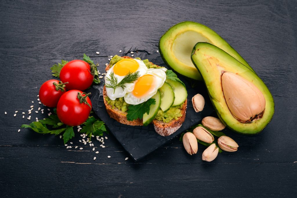 Avocado sandwich with quail eggs, cucumber and pistachios. On a wooden background.