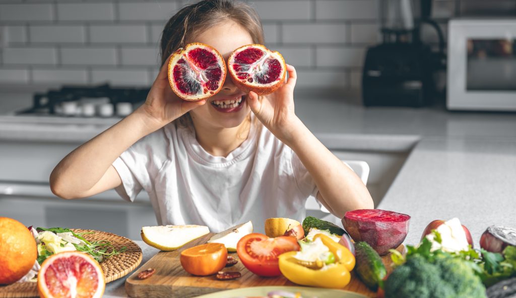 Cheerful little girl with oranges in kitchen interior, healthy eating concept.