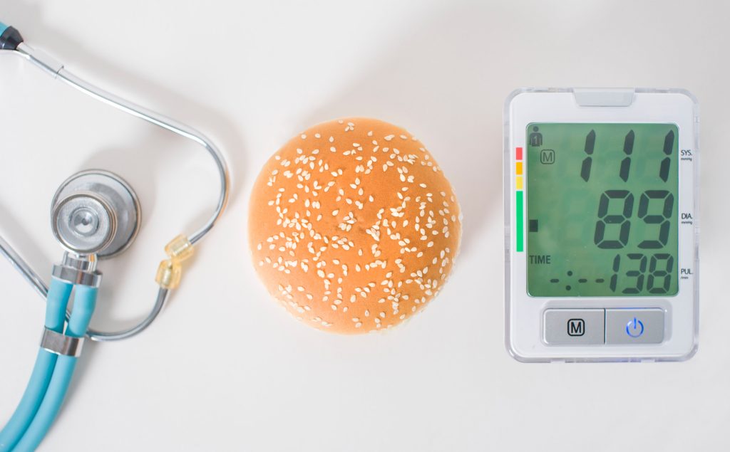 Hamburger, stethoscope and pressure gauge on a white background, top view. Health effects of junk food