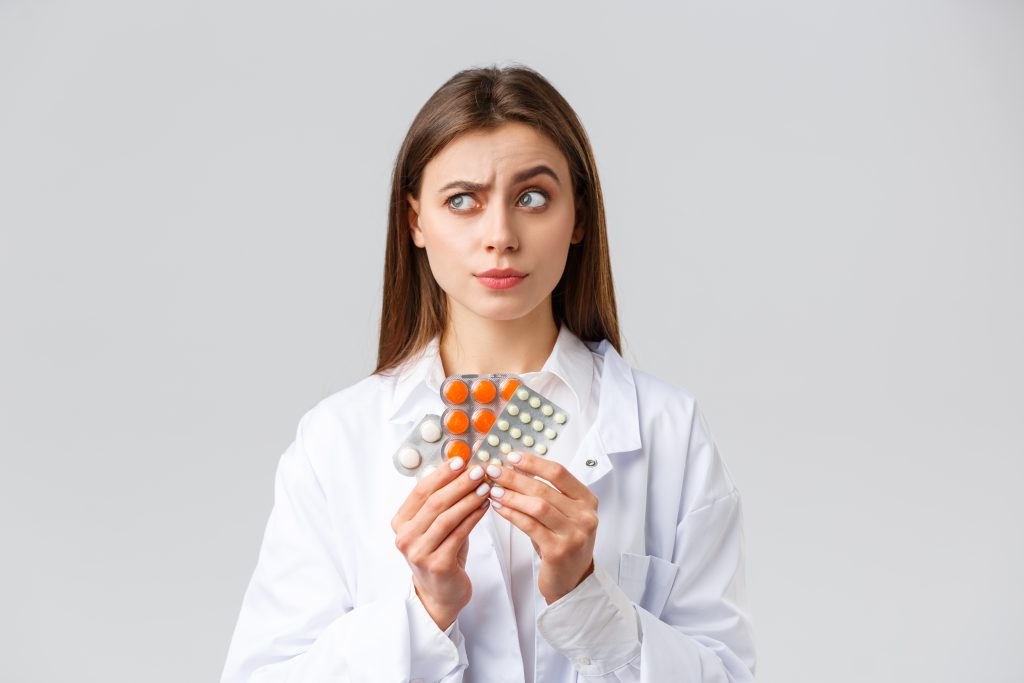 Pharmacy, healthcare workers, insurance and hospitals concept. Thoughtful and skeptical female doctor in white scrubs, look away thinking, consider what pills needed, show medicine.