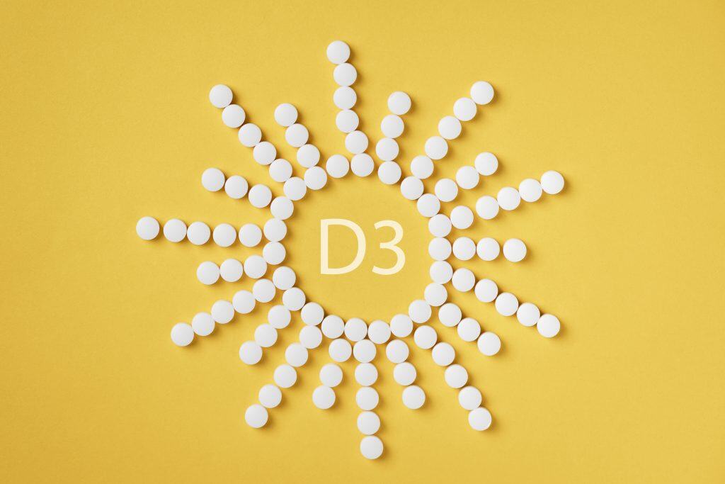 Pills of vitamin D3 in a shape of sun on yellow background top view. Concept of vitamin d3.