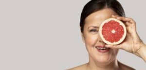 zdjęcie przedstawia kobietę w średnim wieku, która na wysokości twarzy trzyma grejpfrut